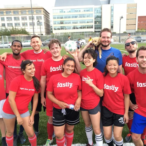 Amy and Fastly coworkers in red team t-shirts on a soccer field, one holding a golden retriever puppy