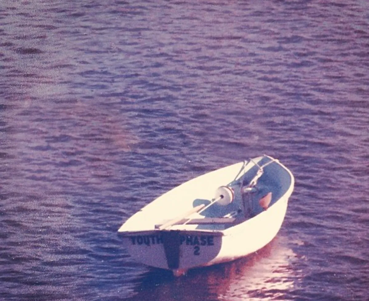 A photo print of Pop's dinghy: a small white boat floating on rippled dusk water, YOUTH PHASE 2 lettered on the bow